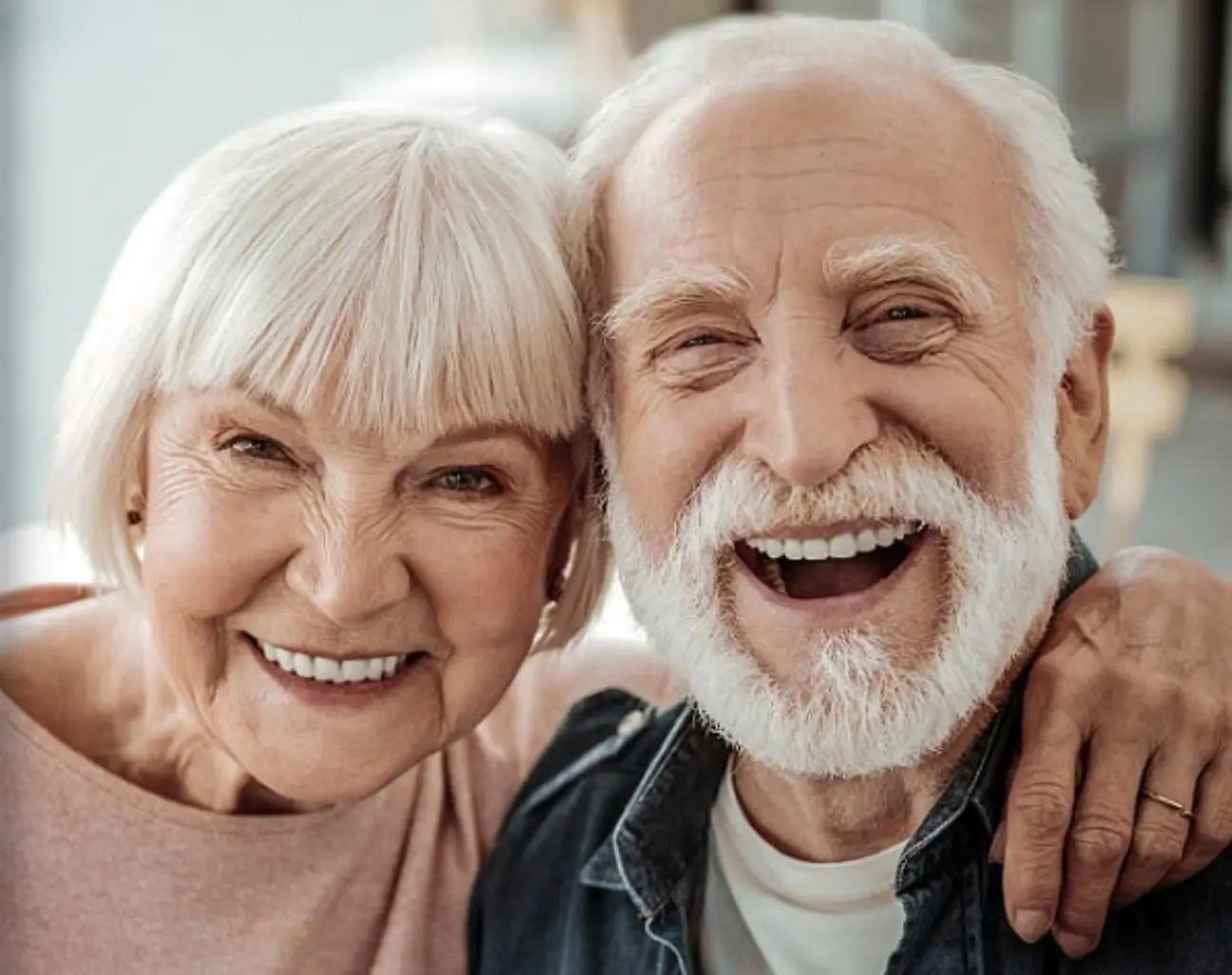 Deux personnes âgées souriant côte à côte, l'une ayant son bras autour des épaules de l'autre.